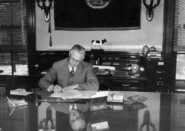 Governor Oscar Rennebohm, seated as his desk and signing a bill